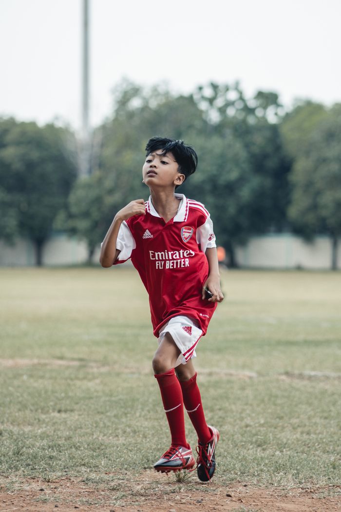 A young boy practicing soccer outdoors in a red sports jersey.